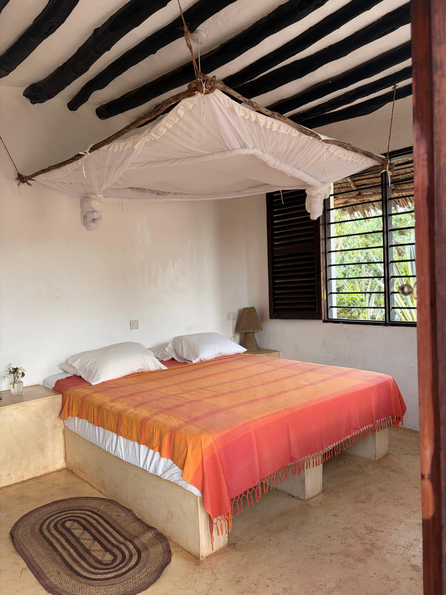 The Nyota room: a low plaster platform bed with a coral and orange kikoi under a hanging mosquito net and black beams