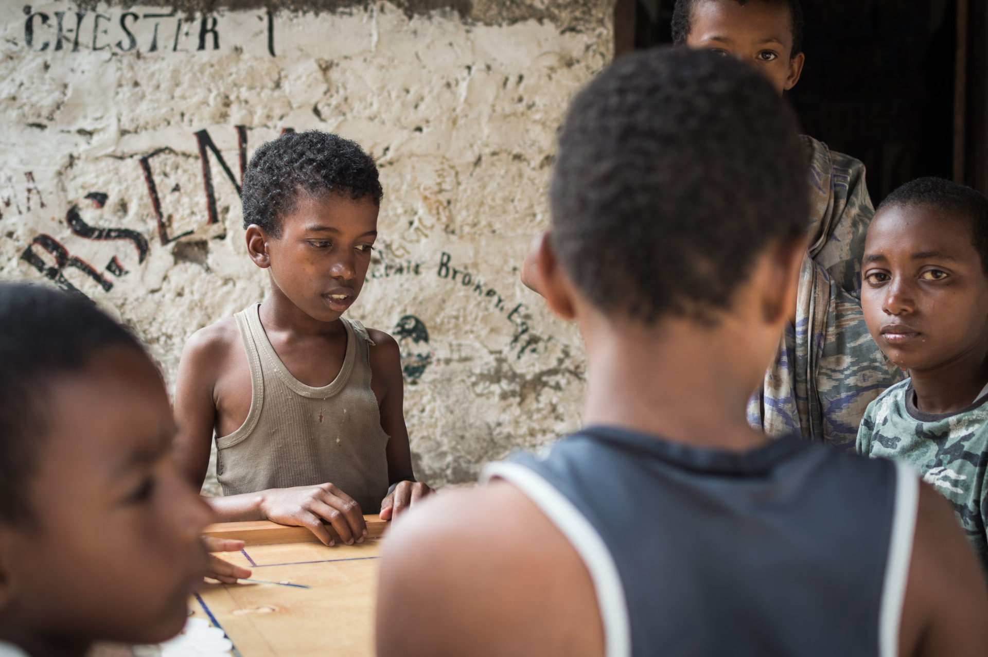 Children gathered around a table game in a shaded lane in Lamu town