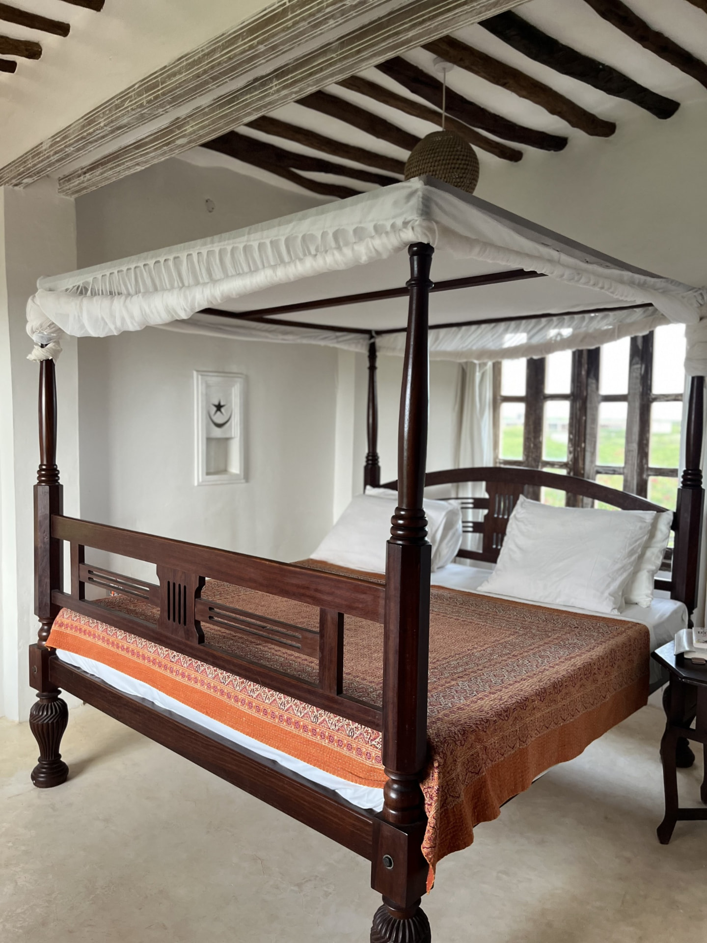 The Mwezi bedroom: a dark wood four-poster bed with a block-printed cover under a beamed ceiling