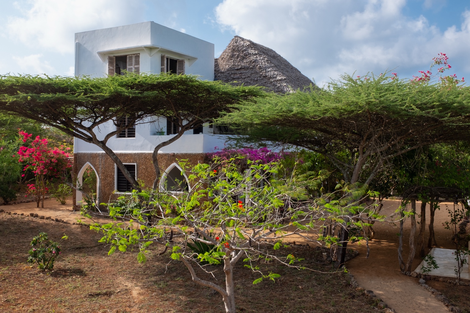Mkoko, a coral stone house with a thatched roof rising above the trees on Manda Island