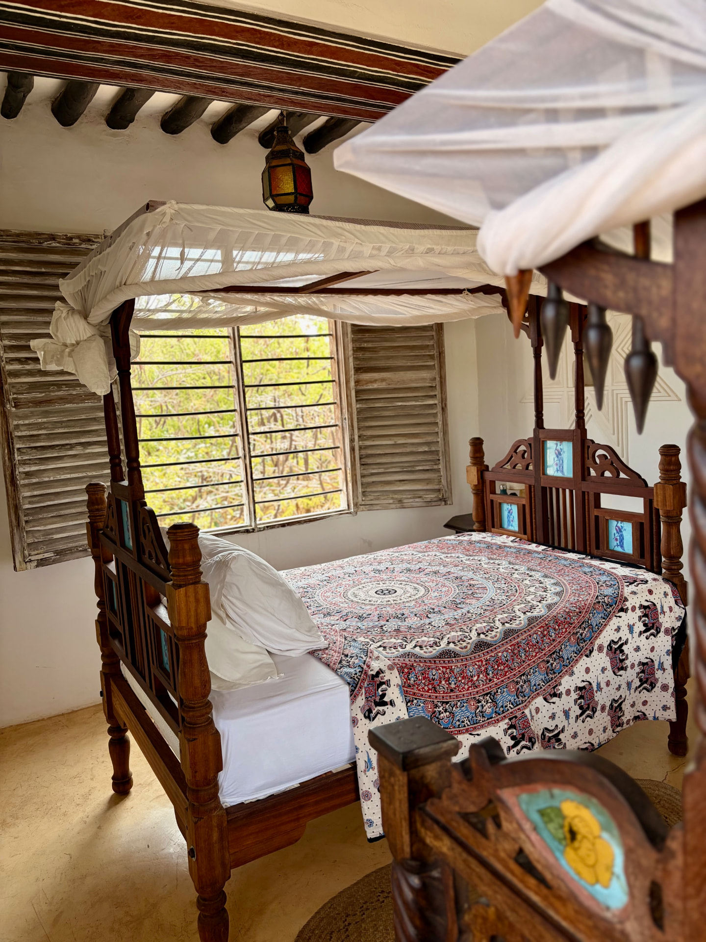 The Mkoko room: a carved four-poster bed with a block-printed cover and mosquito net beneath a painted timber ceiling