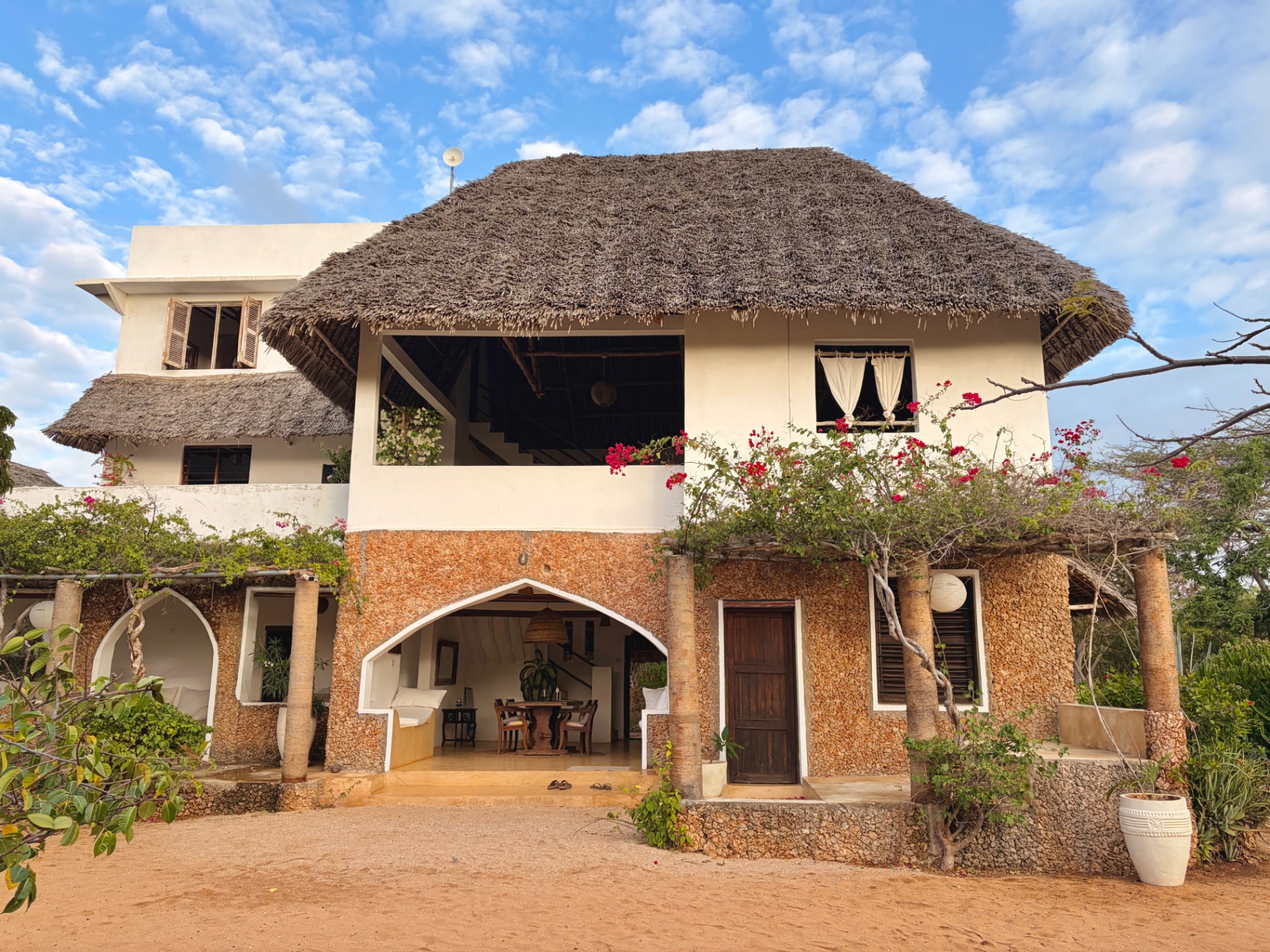 Mkoko House seen from the sandy courtyard, makuti roof above coral-stone arches and bougainvillea