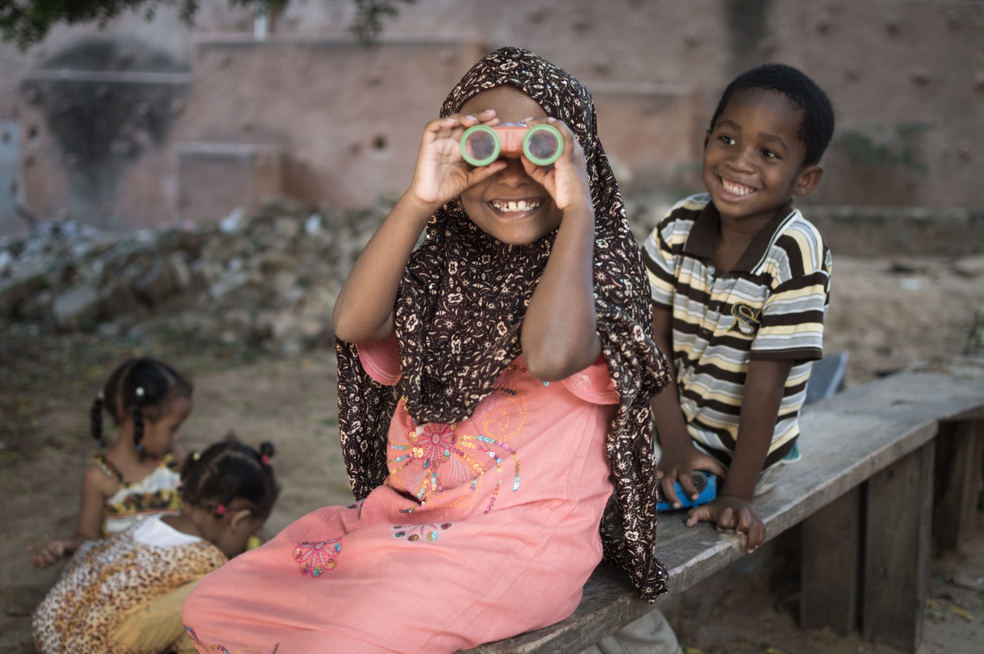 Children in the Lamu archipelago, one smiling through toy binoculars while another laughs beside her