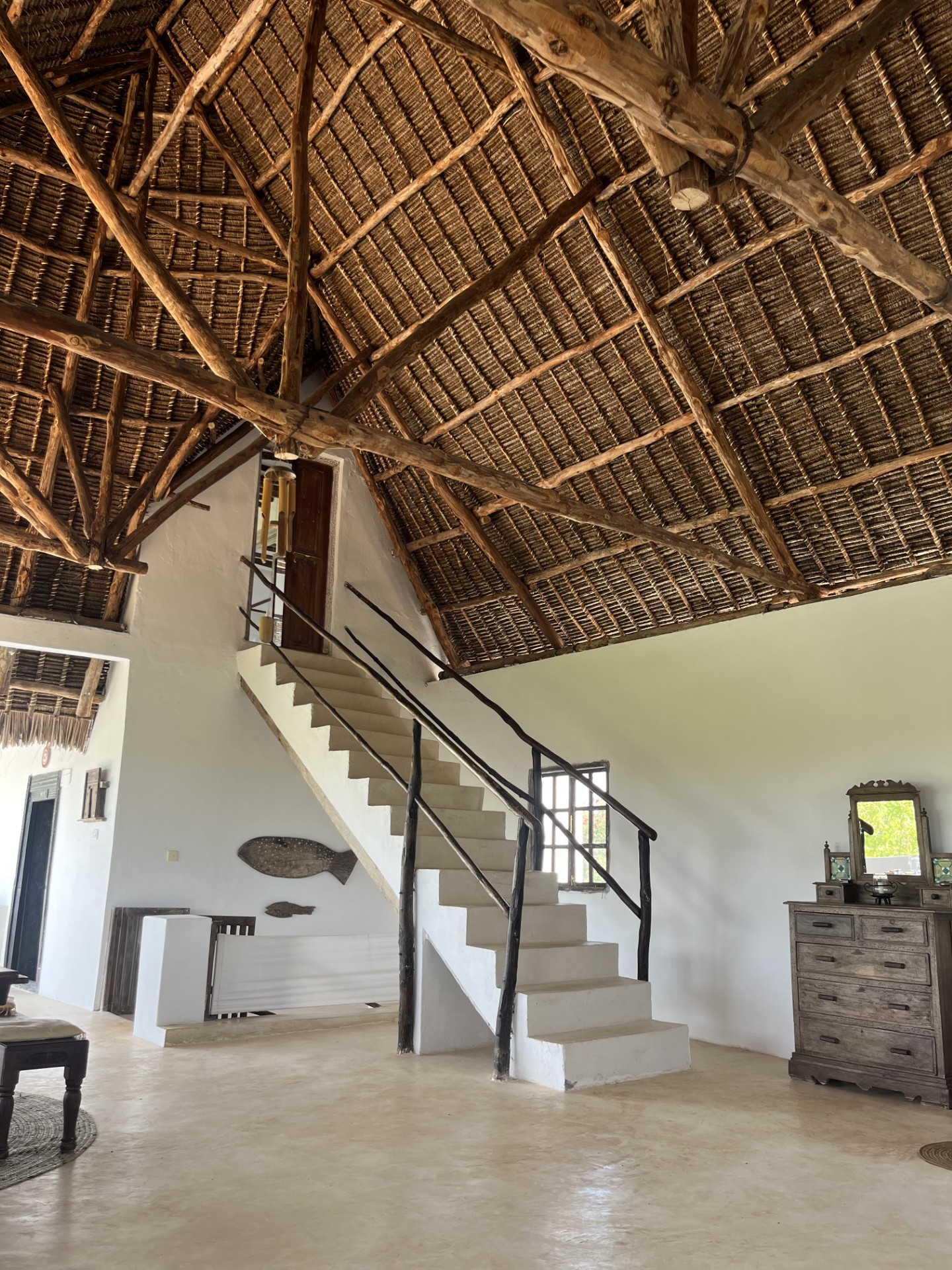 Whitewashed staircase with mangrove-pole railings rising under an exposed timber and thatch roof