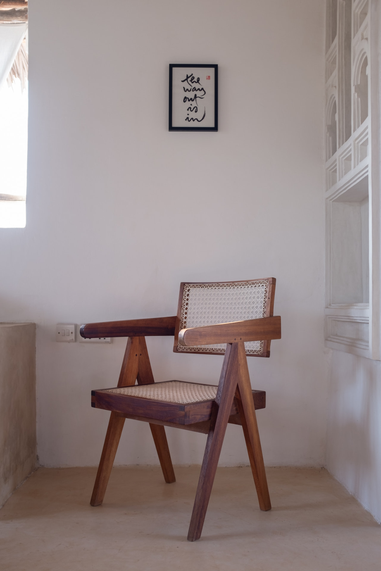A woven cane armchair in a whitewashed corner of Mkoko House beneath a small framed calligraphic print