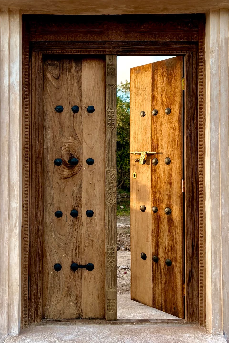 The carved wooden entrance gate at Mkoko House, studded doors standing open in a plaster and coral-stone portal
