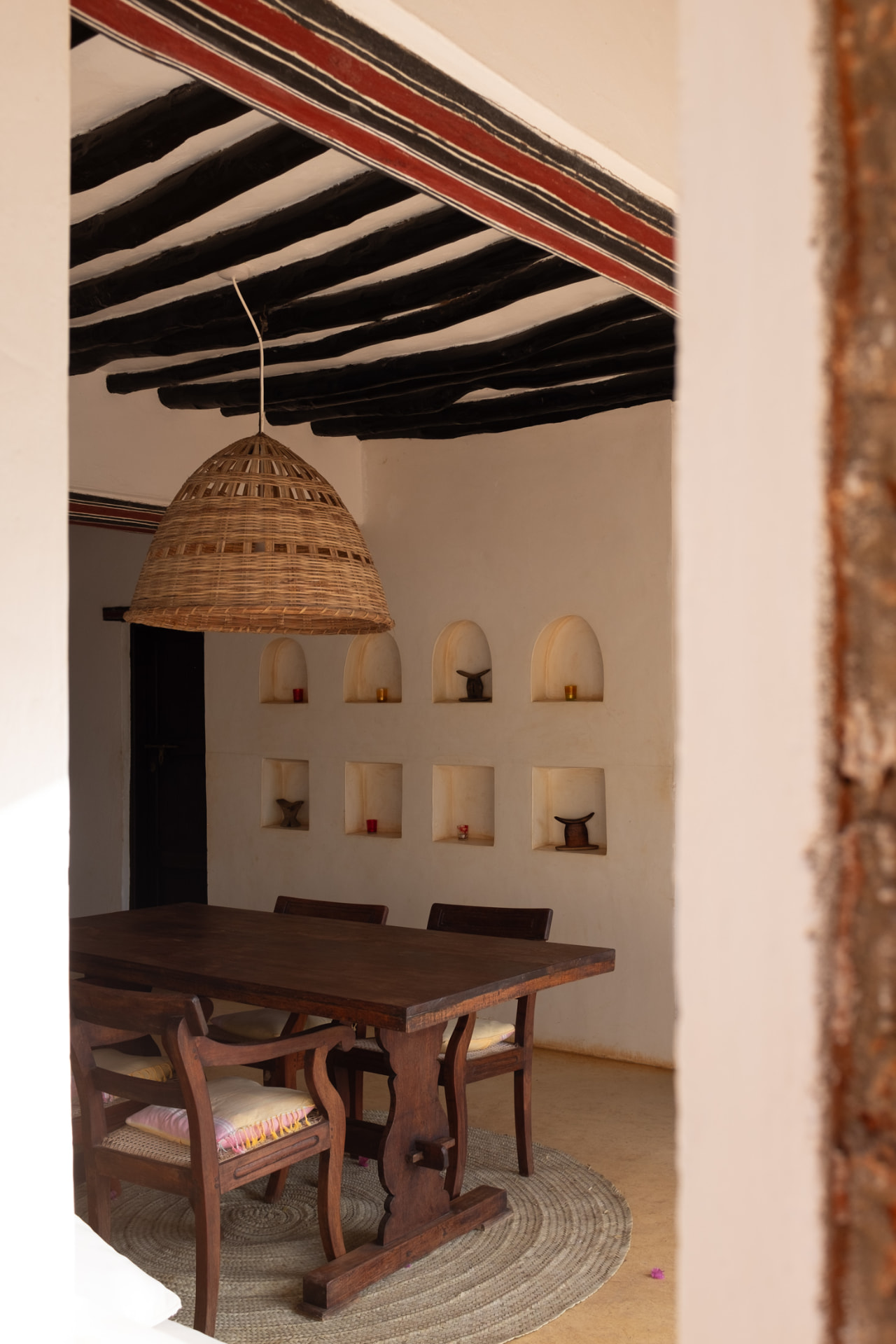 Dining table seen through a thick doorway, with a woven pendant lamp and arched plaster niches behind