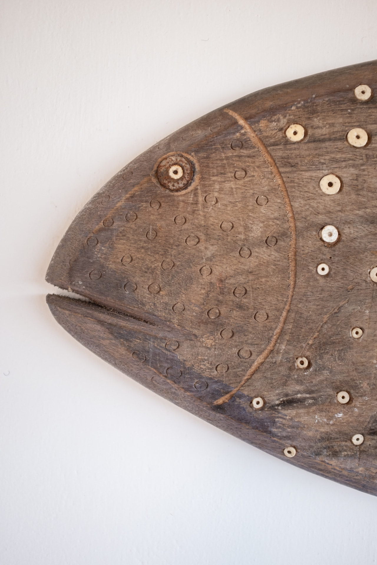 Carved wooden fish with circular shell inlays mounted on a white plaster wall at Mkoko House