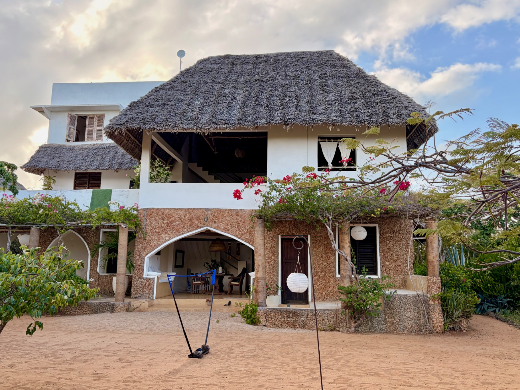 The front of Mkoko House at dusk, its makuti roof and coral-stone arches above the sandy courtyard