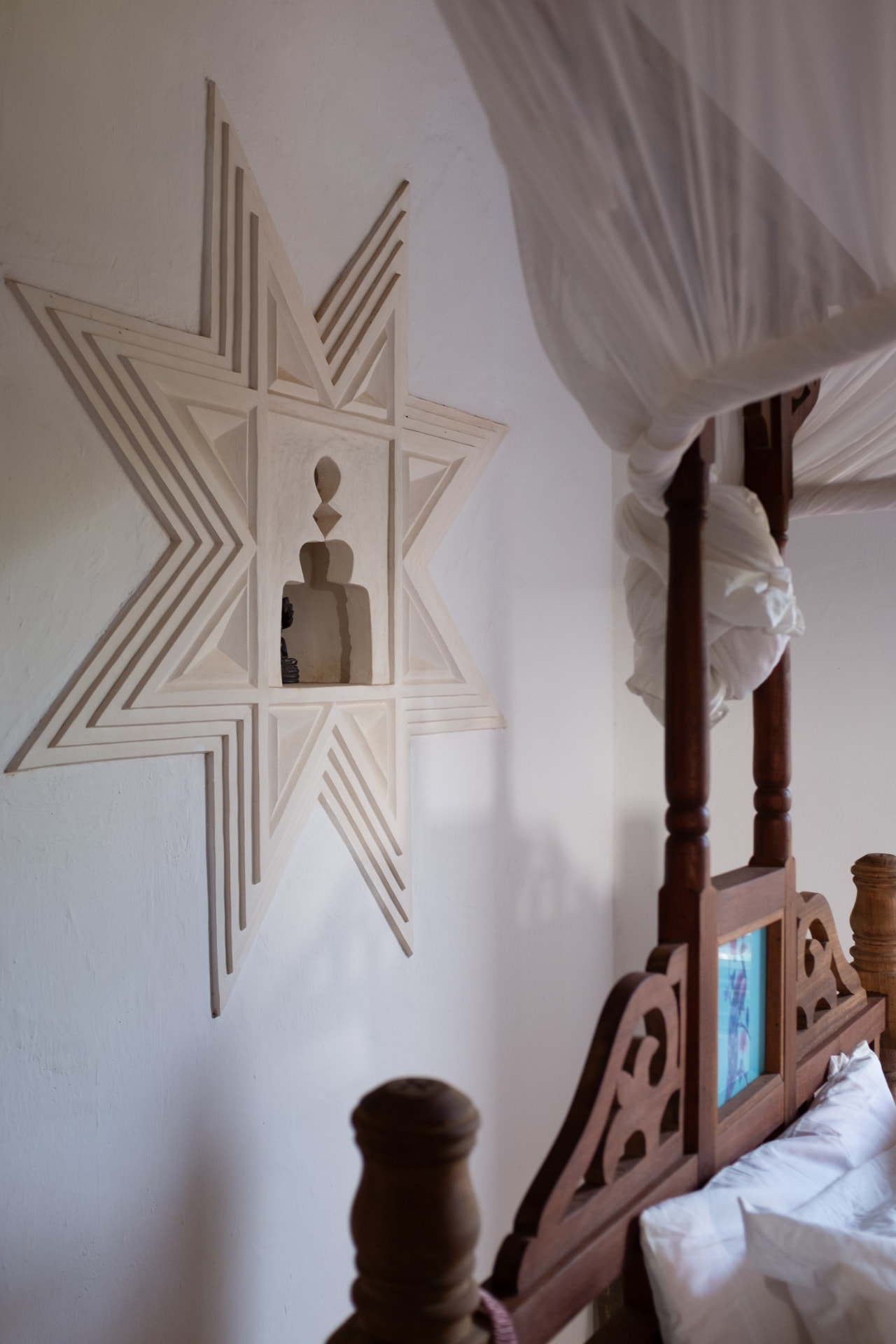 A recessed star-shaped plaster niche beside a dark wood bed frame and white mosquito netting