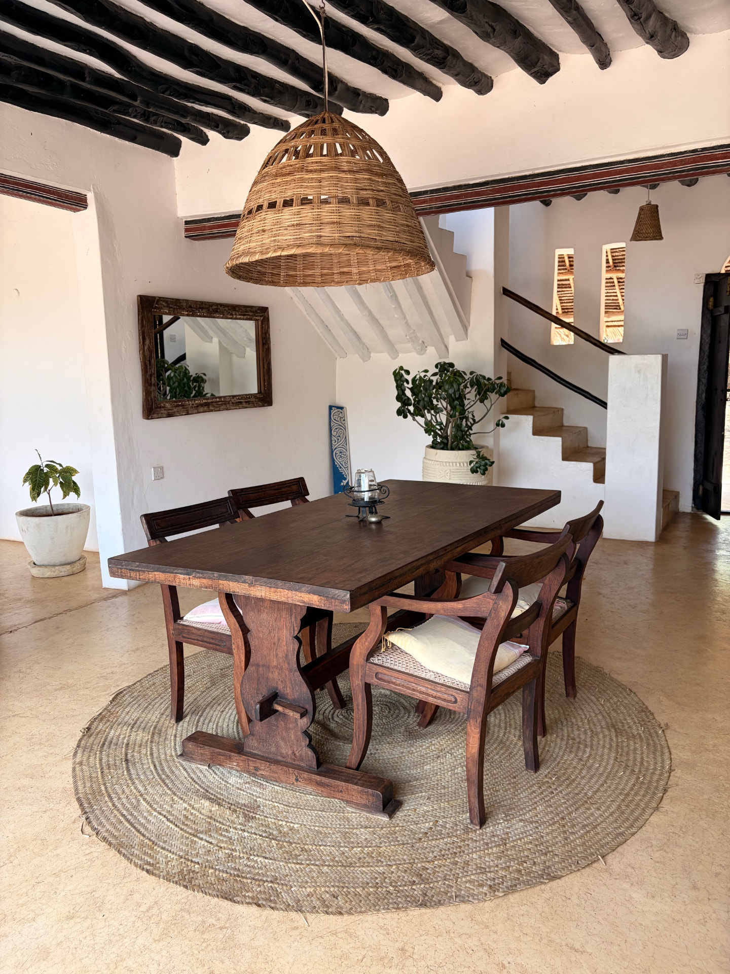 Downstairs dining room at Mkoko House with a heavy timber table under a woven pendant lamp and whitewashed staircase