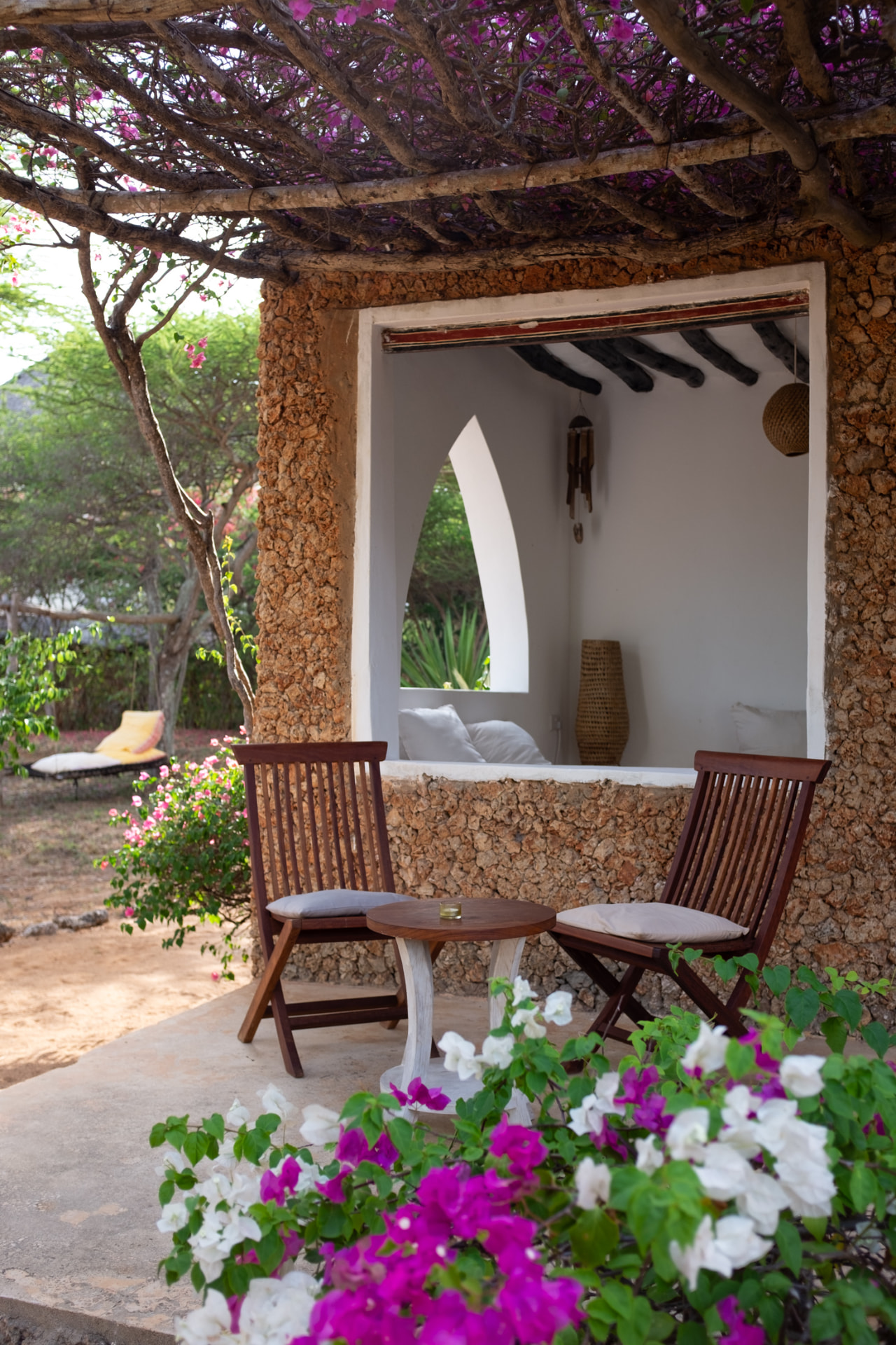 Two wooden chairs and a small table on the coral-stone veranda at Mkoko House, under a bougainvillea-covered pergola