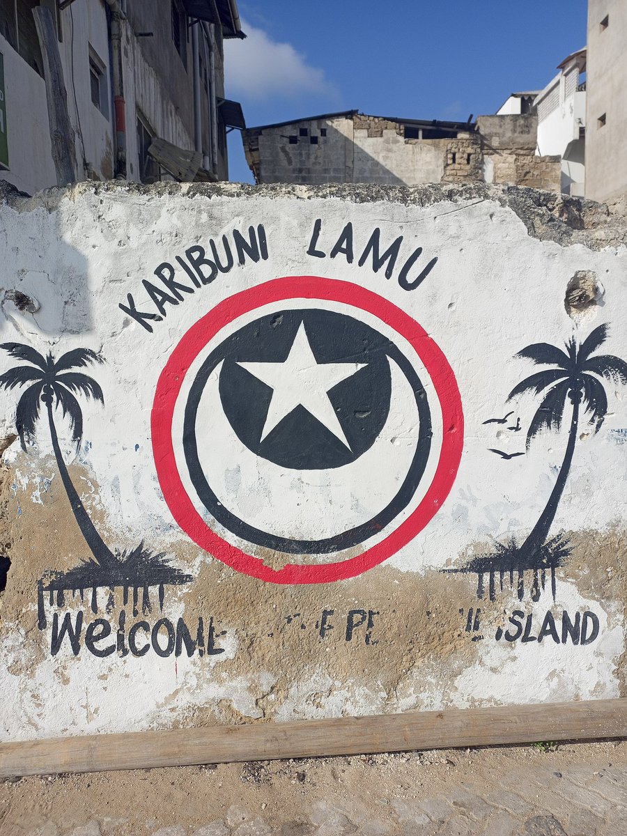 A painted wall in Lamu reading Karibuni Lamu, with a star and crescent between two palm trees
